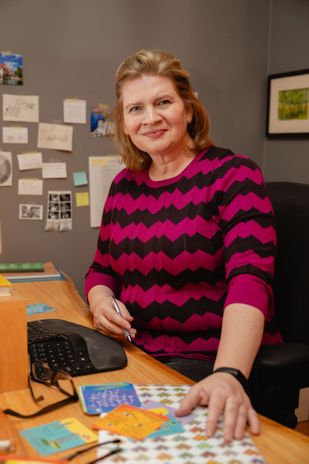 Emmy Laybourne at her writing desk, pen in hand, smiling at the camera
