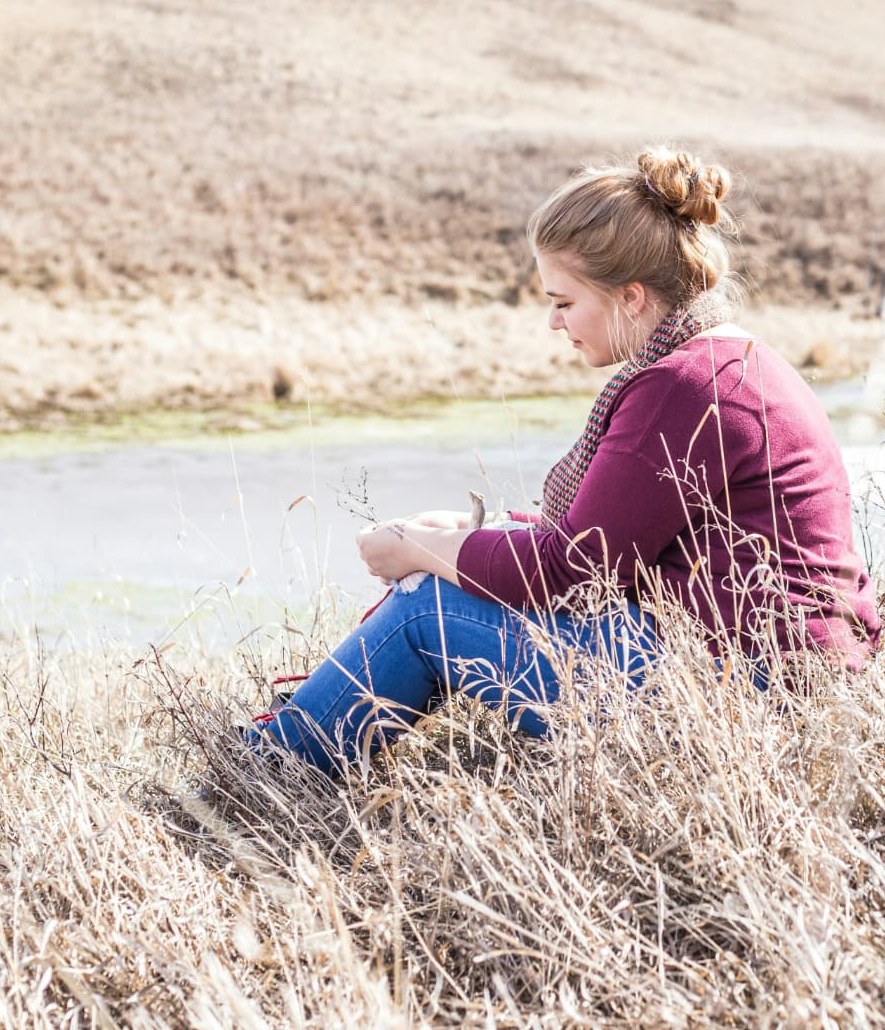 A woman sitting quietly in tall grass by a stream
